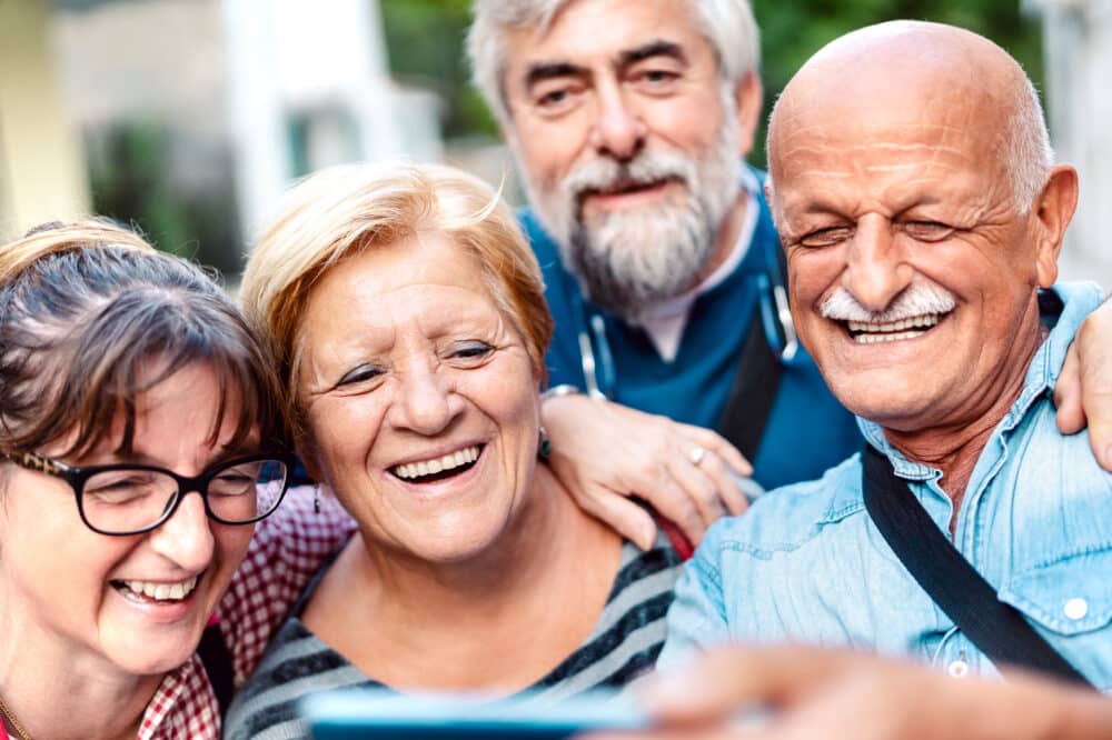 Senior living. Happy senior friends taking selfie around old town street - Retired people having fun together with mobile phone - Positive elderly lifestyle concept with focus on blond woman