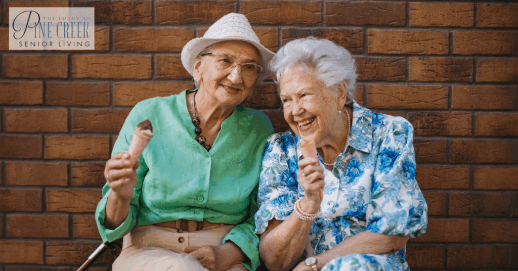 Two elderly women happily enjoying ice cream cones together while sitting outside. Their light clothing and joyful expressions highlight the importance of social interaction and cooling activities when caring for people with dementia in warm temperatures.