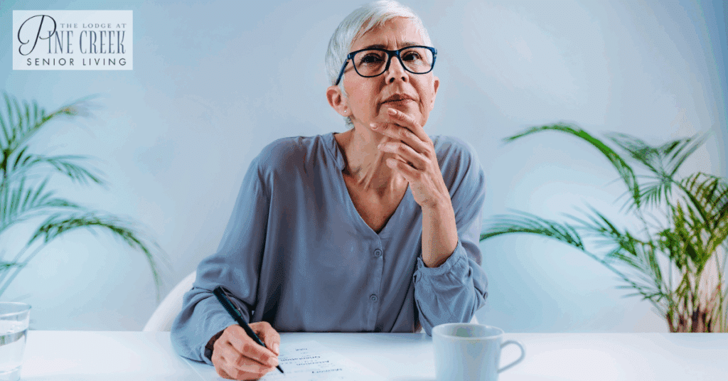 An elderly woman sits thoughtfully at a table, reflecting on her loved one's living arrangement. Her expression shows deep concentration as she considers the best options, possibly weighing memory care vs assisted living