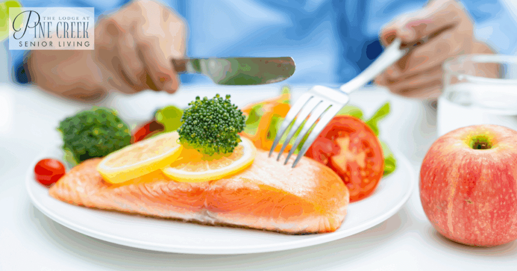 An elderly woman enjoys a nutritious meal of salmon, broccoli, and vegetables. This scene reflects the lifestyle differences between memory care vs assisted living, where nutrition and well-being are key considerations in both settings
