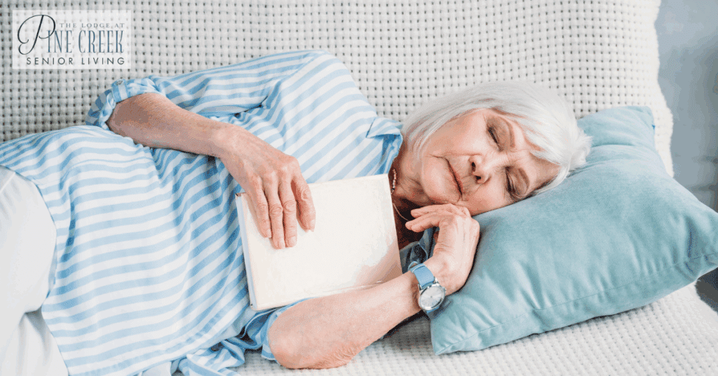 An elderly woman with dementia sleep problems is lying on a sofa, holding a book while resting. She appears to have dozed off, suggesting daytime sleepiness or disrupted sleep patterns.
